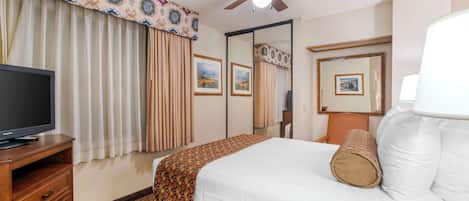 A hotel room with a bed, a television, a ceiling fan, and a large mirror.
