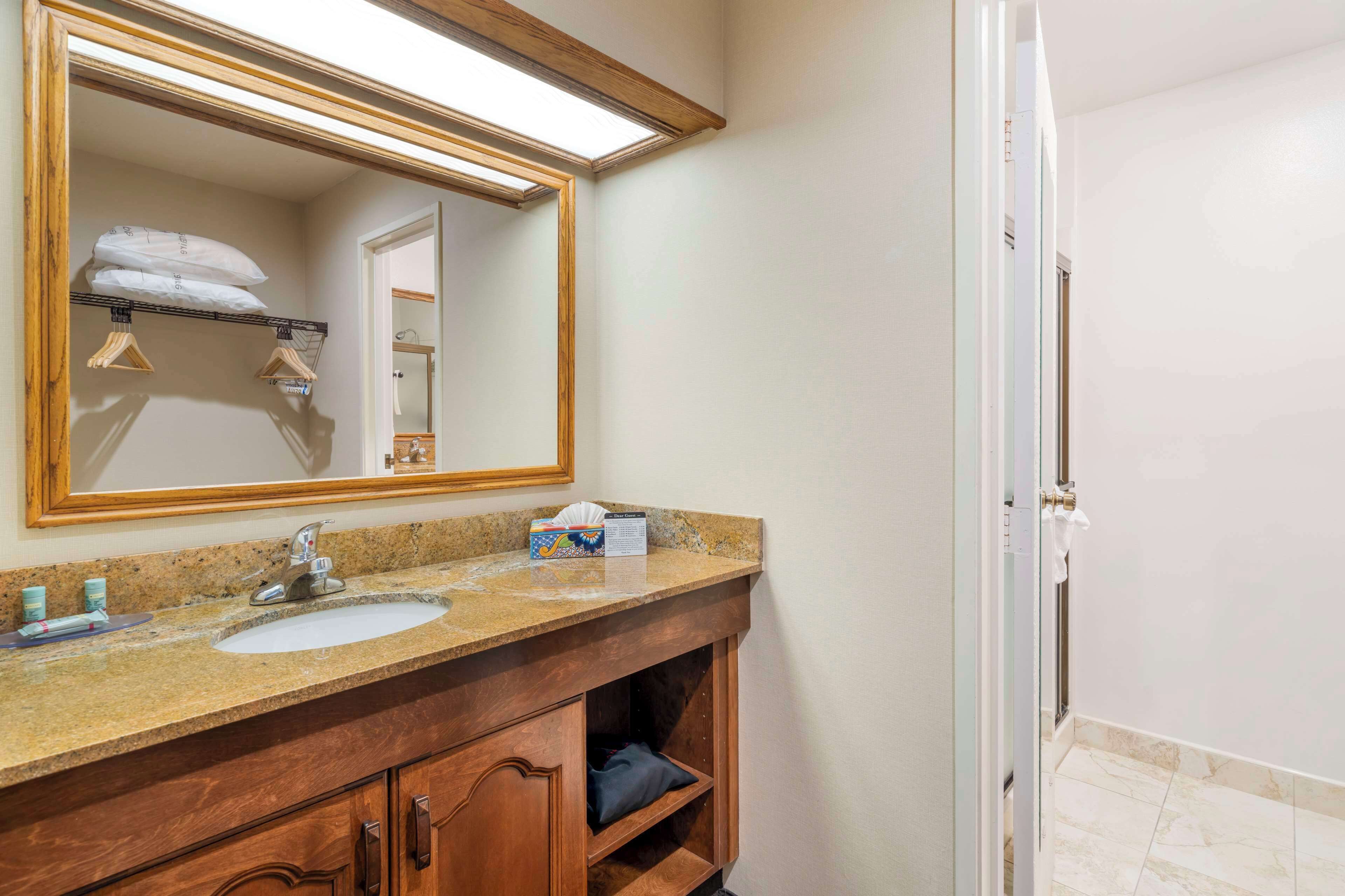 A bathroom with a wooden vanity, a large mirror, a sink, and a shower area.