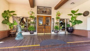 A hotel entrance with a wooden double door, large potted plants, and a tiled floor. - Best Western Casa Grande Inn (Pismo Beach)