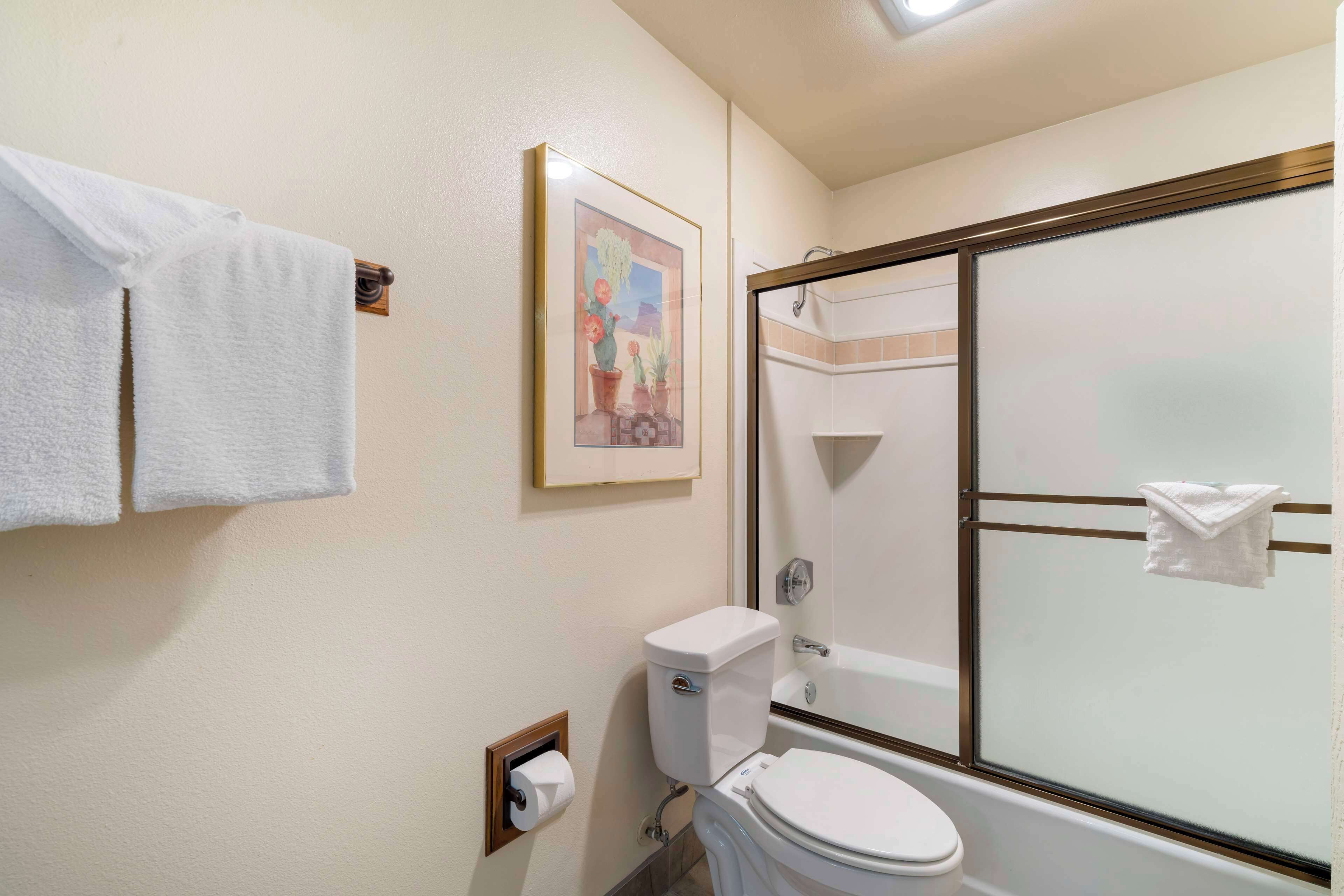 Et badeværelse med toilet, en brusekabine med glasvægge og et billede i ramme på væggen.