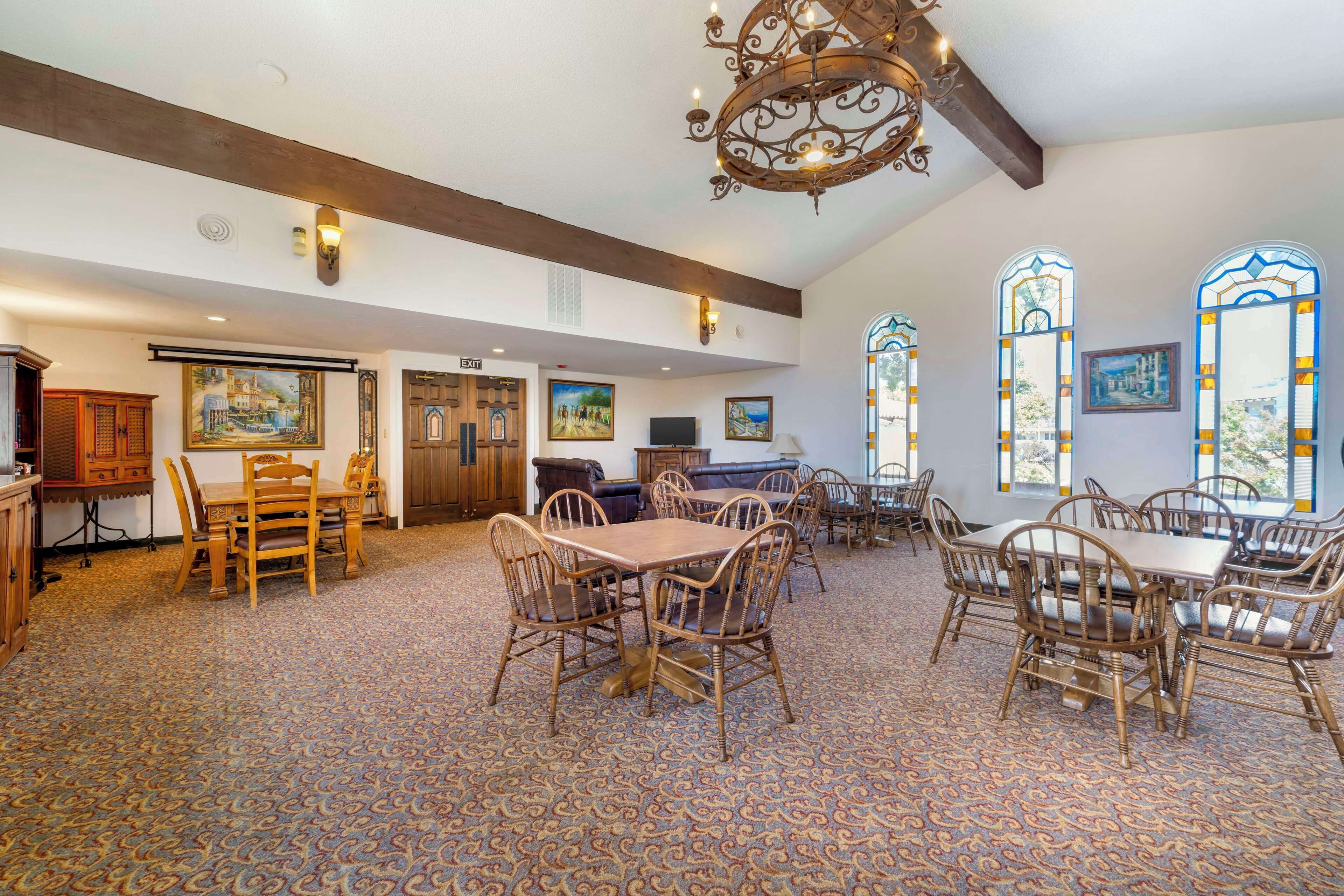 A spacious dining area with wooden tables and chairs, a patterned carpet, and large windows with stained glass.