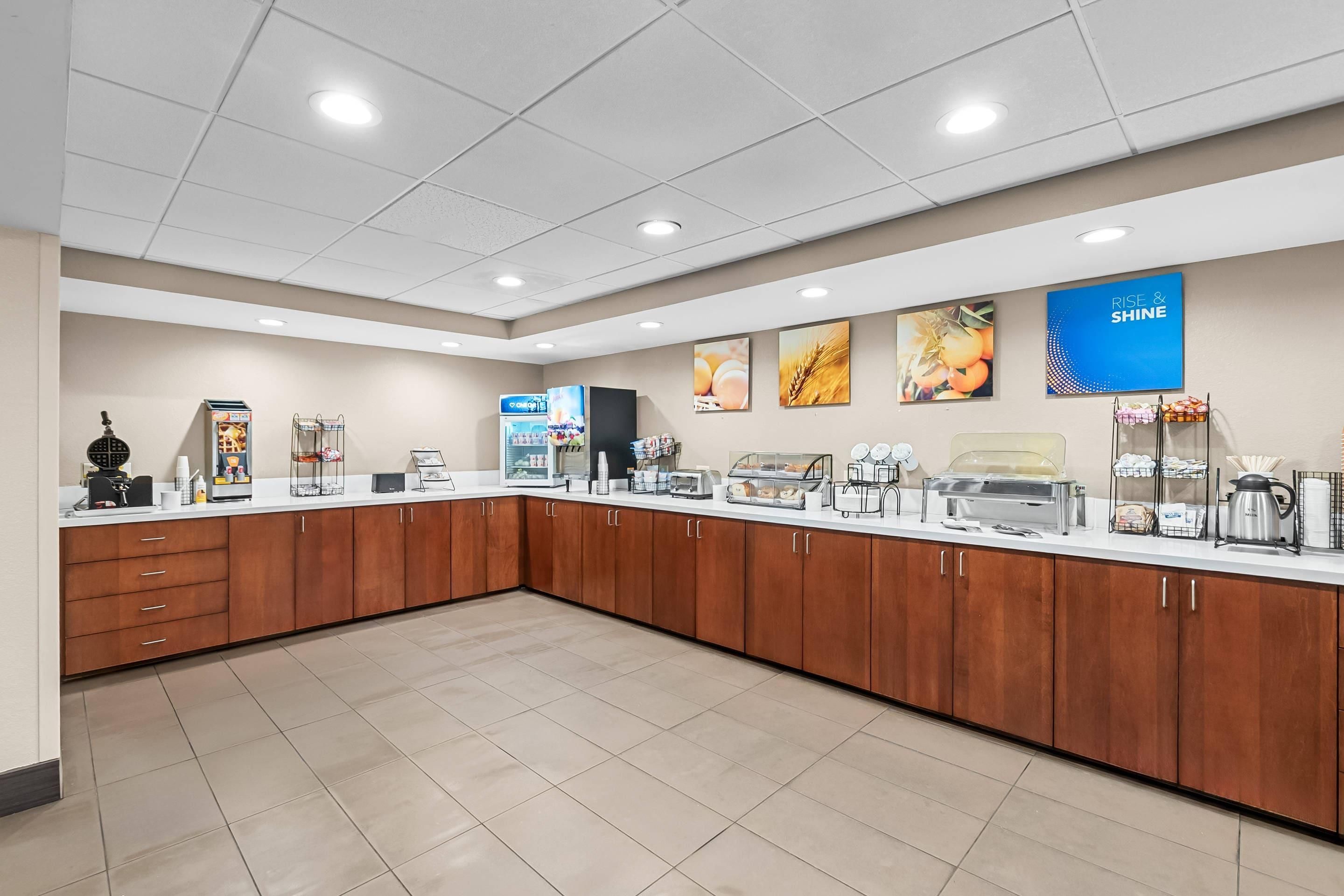 Uma área de pequeno-almoço self-service com diversas opções de comida, uma máquina de café e um frigorífico.