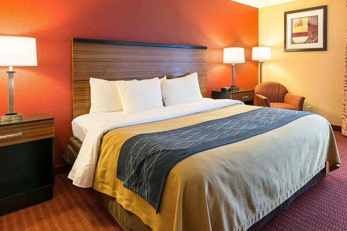 Ein Hotelzimmer mit einem großen Bett, zwei Nachttischen mit Lampen, einem Sessel und einem gerahmten Bild an der Wand.