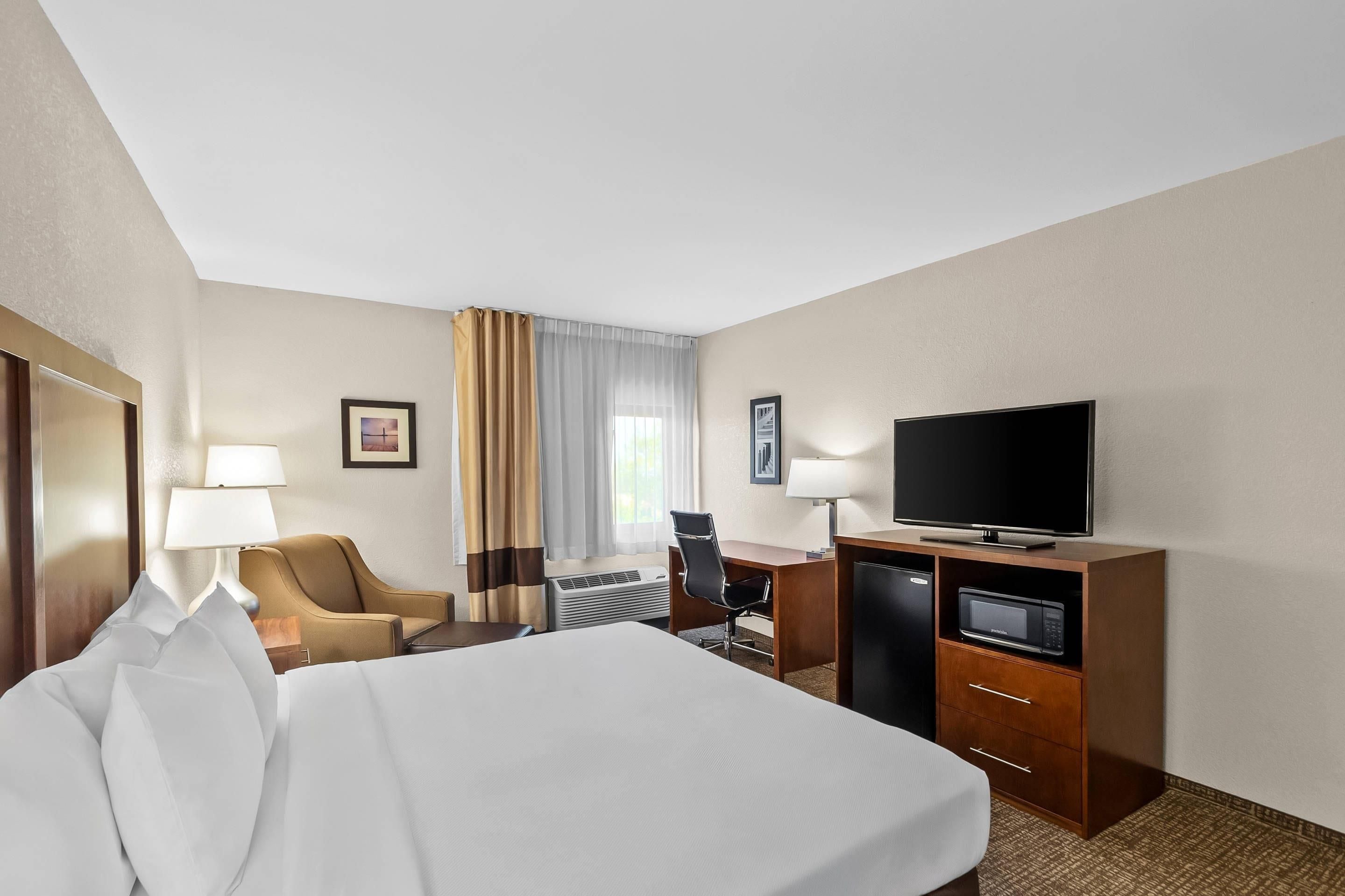 A hotel room with a bed, a desk with a television, a chair, and a lamp.