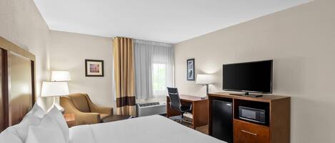 A hotel room with a bed, a desk with a television, a chair, and a lamp.