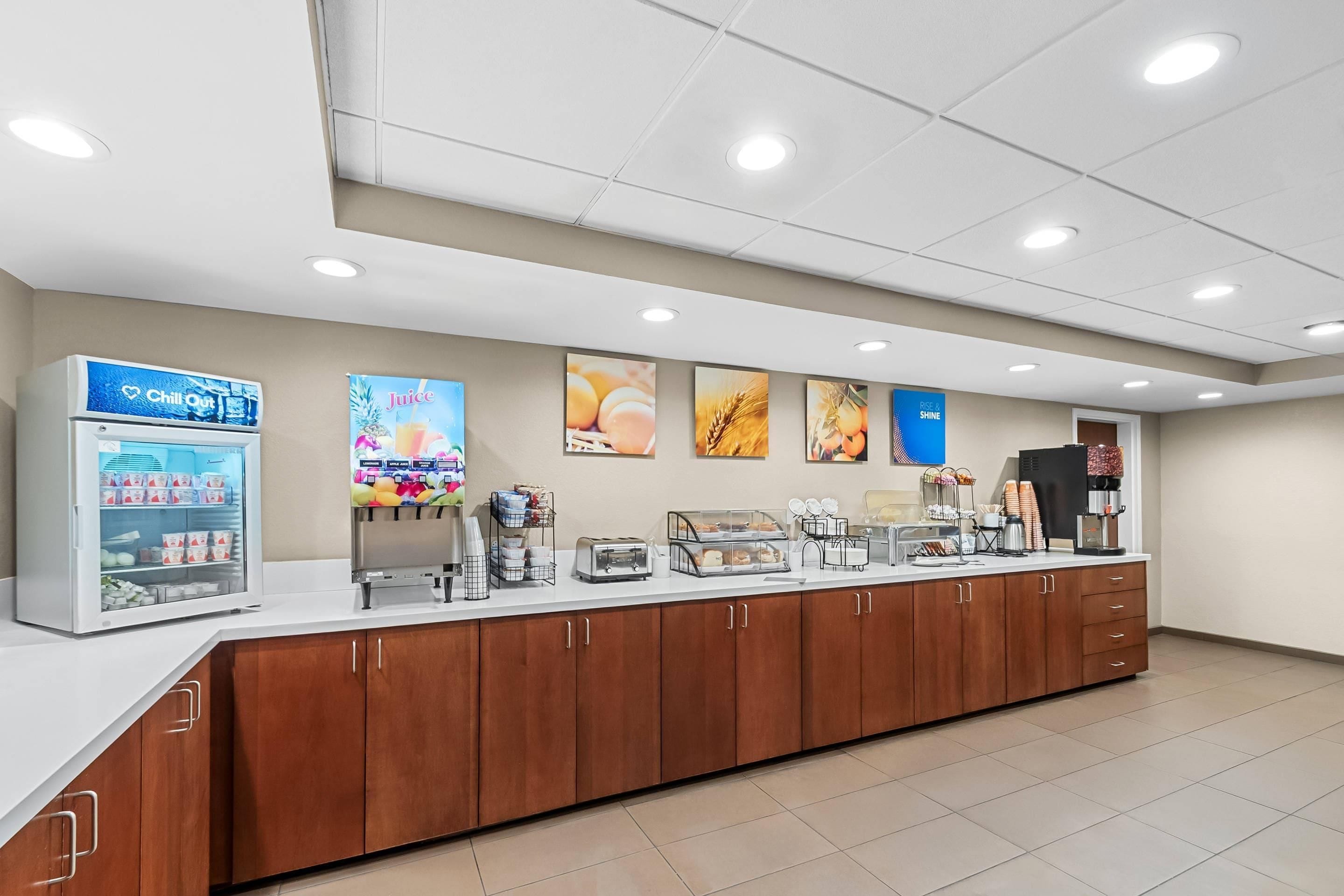 Uma área de café da manhã com serviço próprio, bebidas refrigeradas, um dispensador de suco e diversas opções de alimentos.