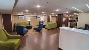 A hotel lobby with green and blue seating, a reception desk, and framed pictures on the walls.
