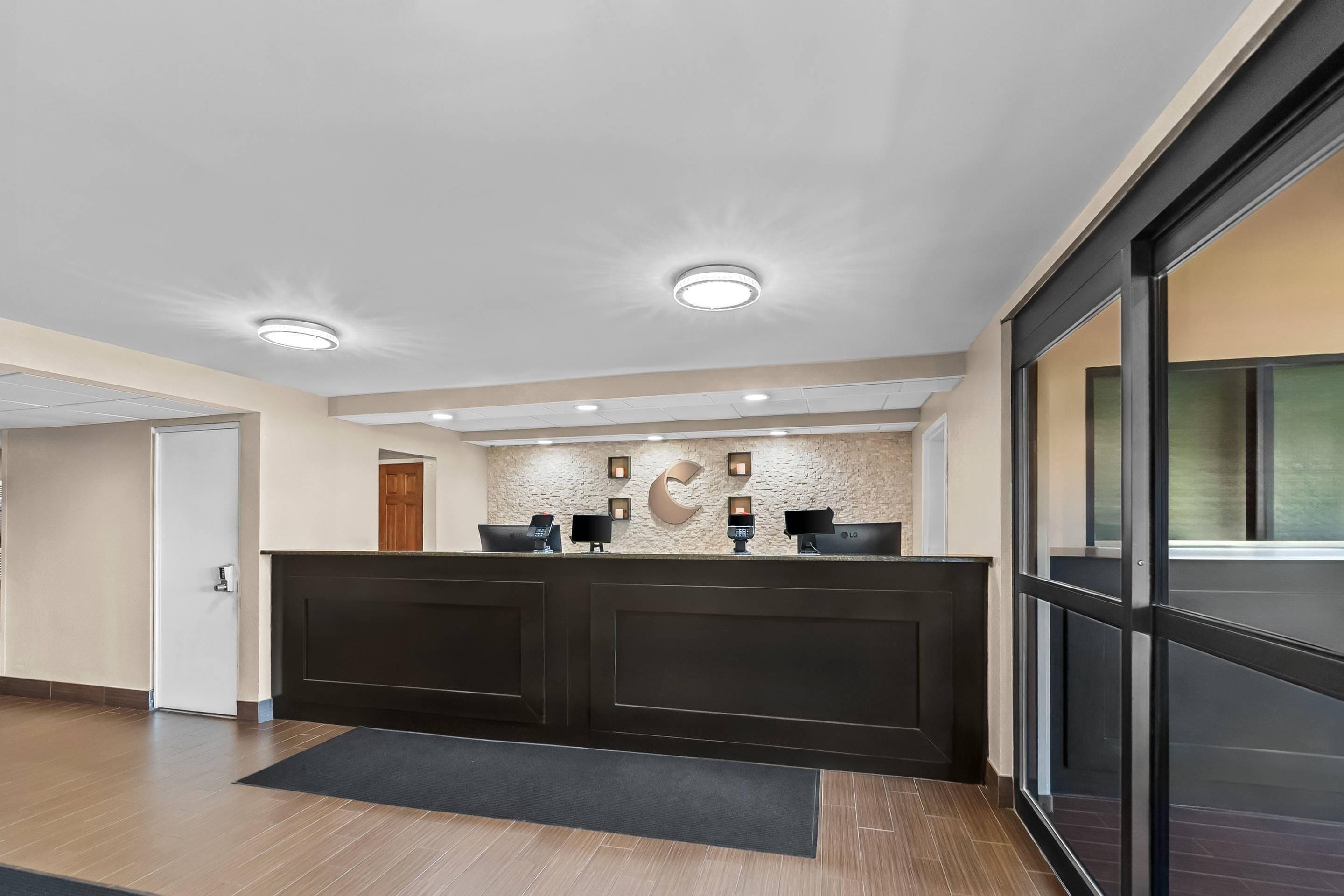 A reception area with a dark reception desk, a wall-mounted counter, and a door leading to another room.