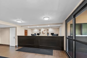 A reception area with a dark reception desk, a wall-mounted counter, and a door leading to another room.