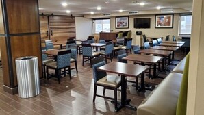 A hotel dining area with multiple tables and chairs, wooden paneling on the walls, and a trash can.
