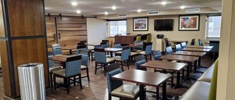 A hotel dining area with multiple tables and chairs, wooden paneling on the walls, and a trash can.