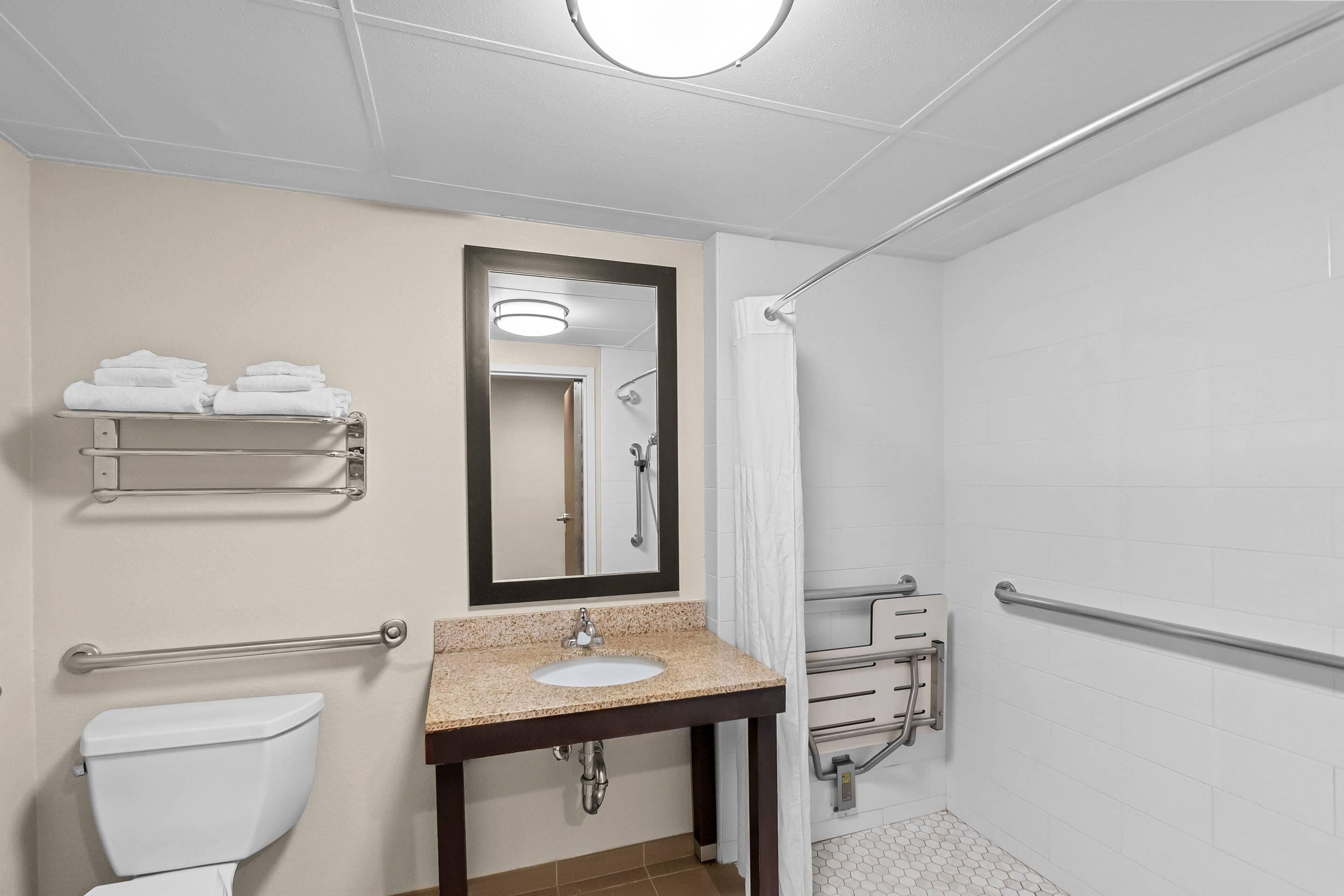 A bathroom with a toilet, sink, mirror, towel rack, and shower area.