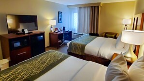 A hotel room with two beds, a desk, a television, and a window with curtains.