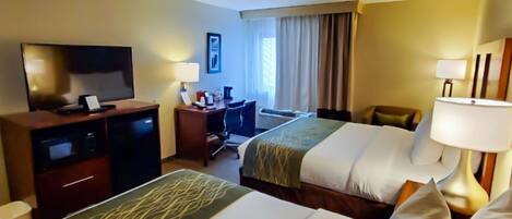 A hotel room with two beds, a desk, a television, and a window with curtains.