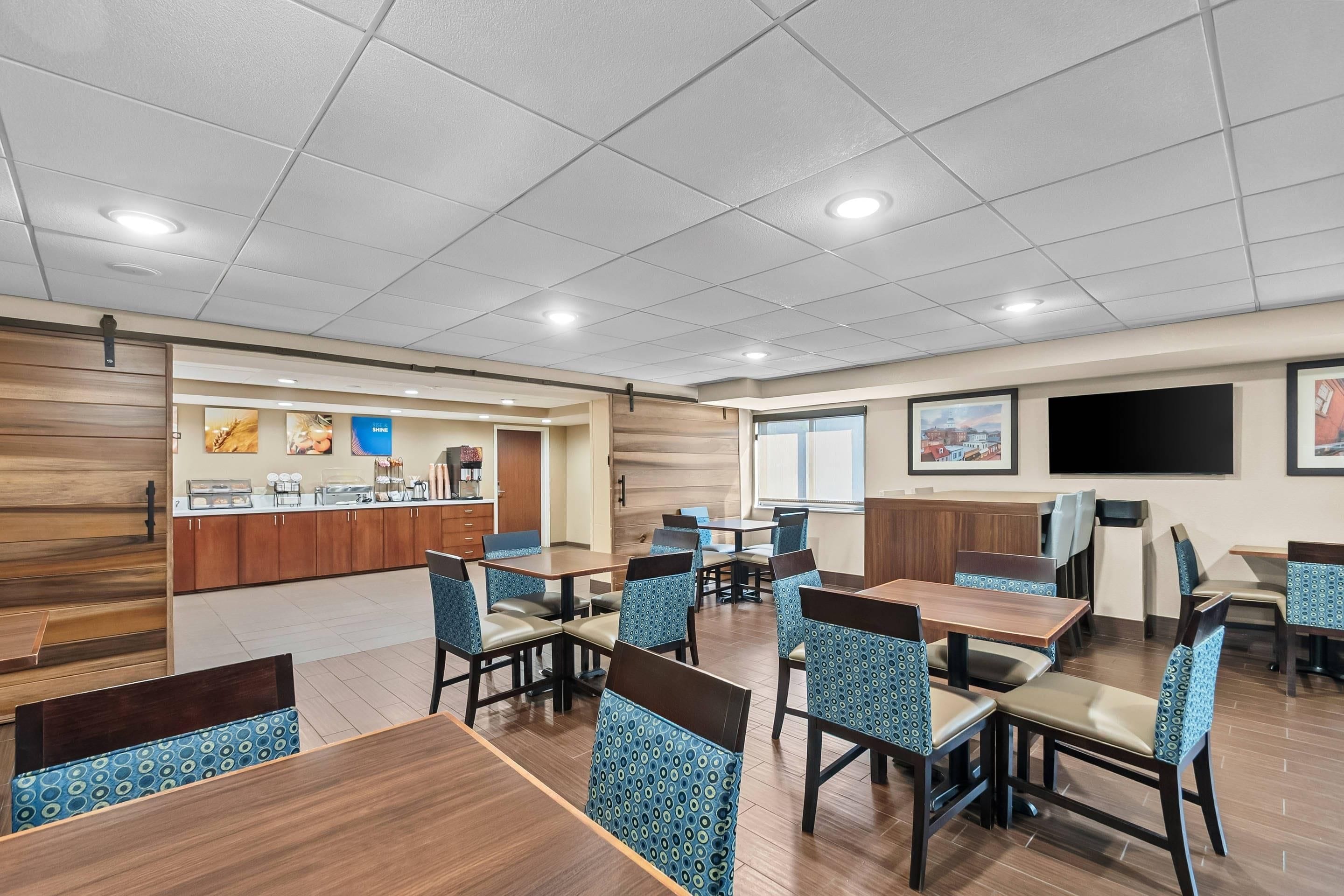A hotel dining area with multiple tables and chairs, a counter with food service, and artwork on the walls.