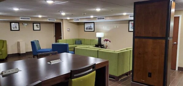 A conference room with a wooden table, blue and green chairs, and a green sofa. - Comfort Inn Oxon Hill - National Harbor (Oxon Hill)
