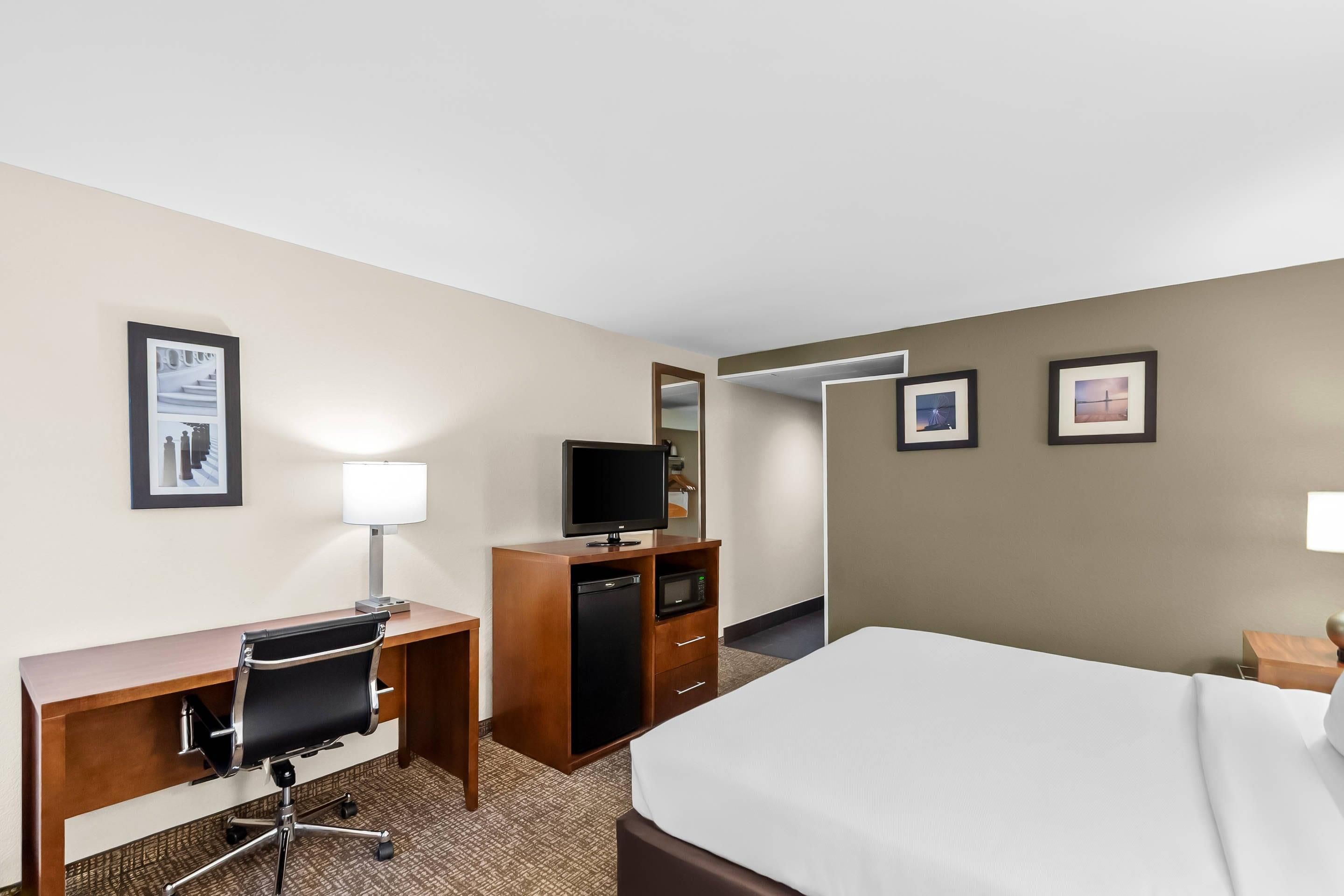 A hotel room with a bed, desk, chair, television, and a microwave.