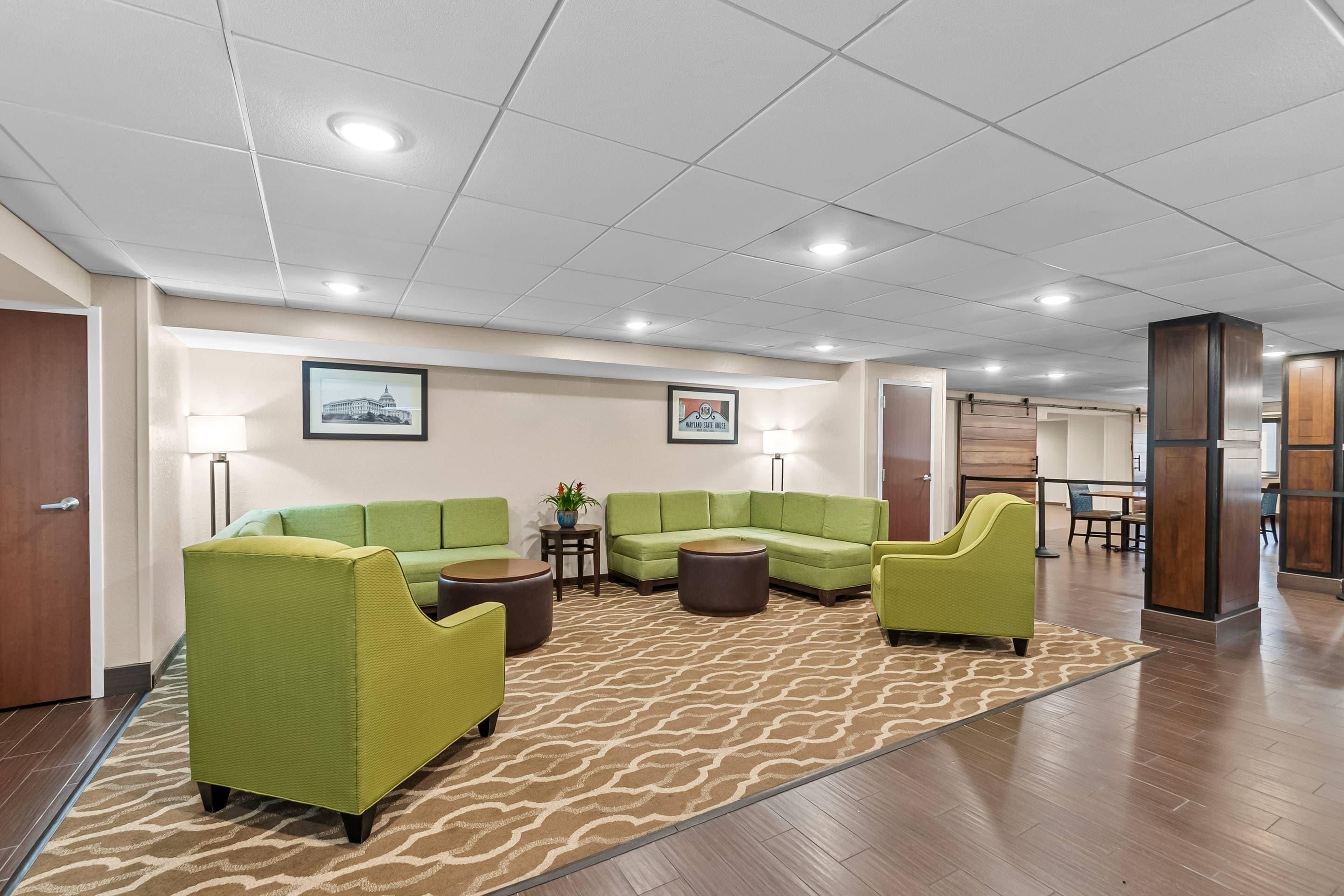 A hotel lobby with green sofas, a patterned rug, and a framed picture of a building.