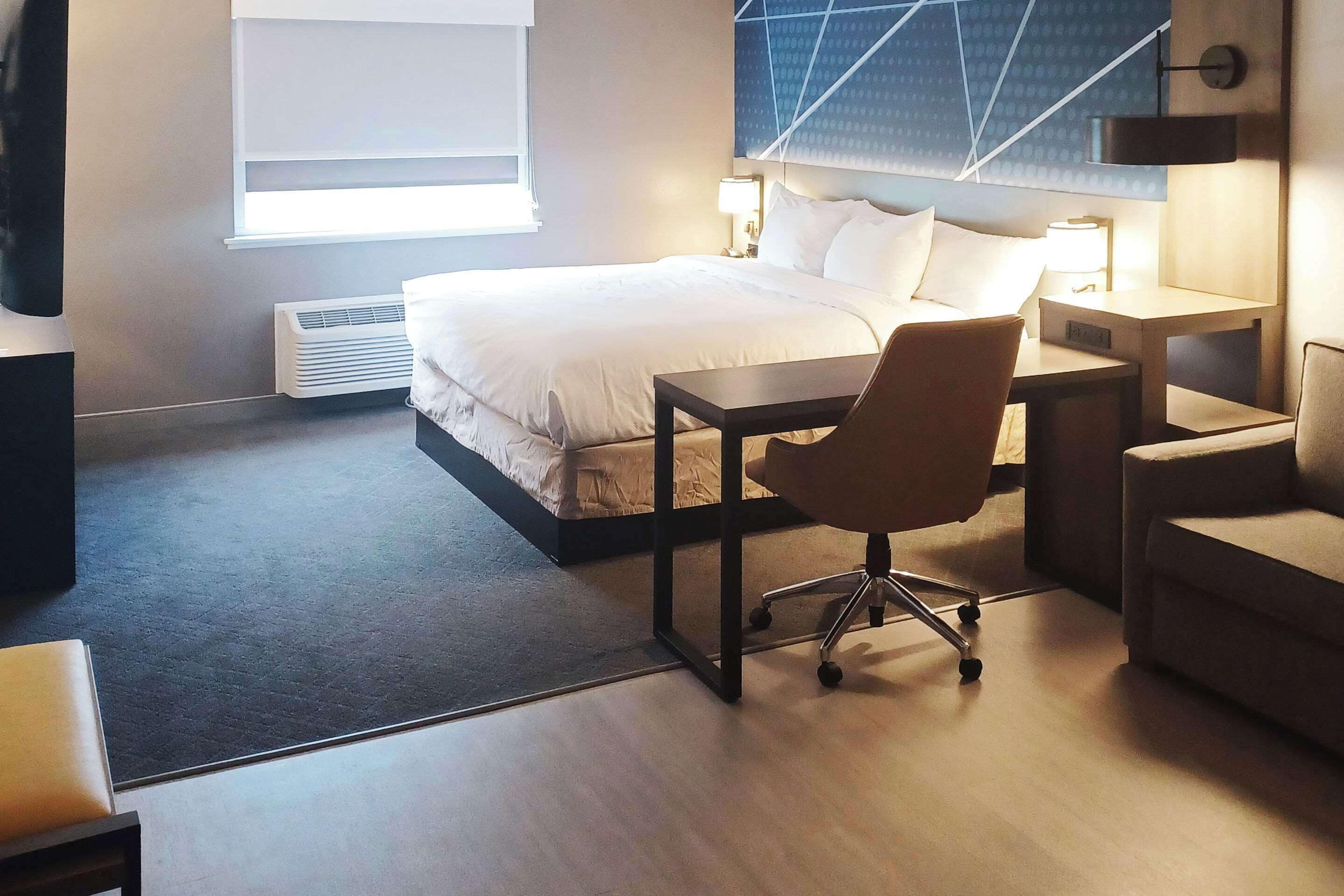 A modern hotel room with a large bed, a desk, a chair, and a sofa.