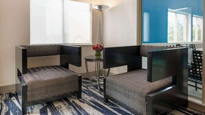 A corner room with two black chairs with patterned cushions, a small round table with a vase of flowers, and a large window with a view of trees. - Comfort Inn Edinburgh - Columbus (Edinburgh)