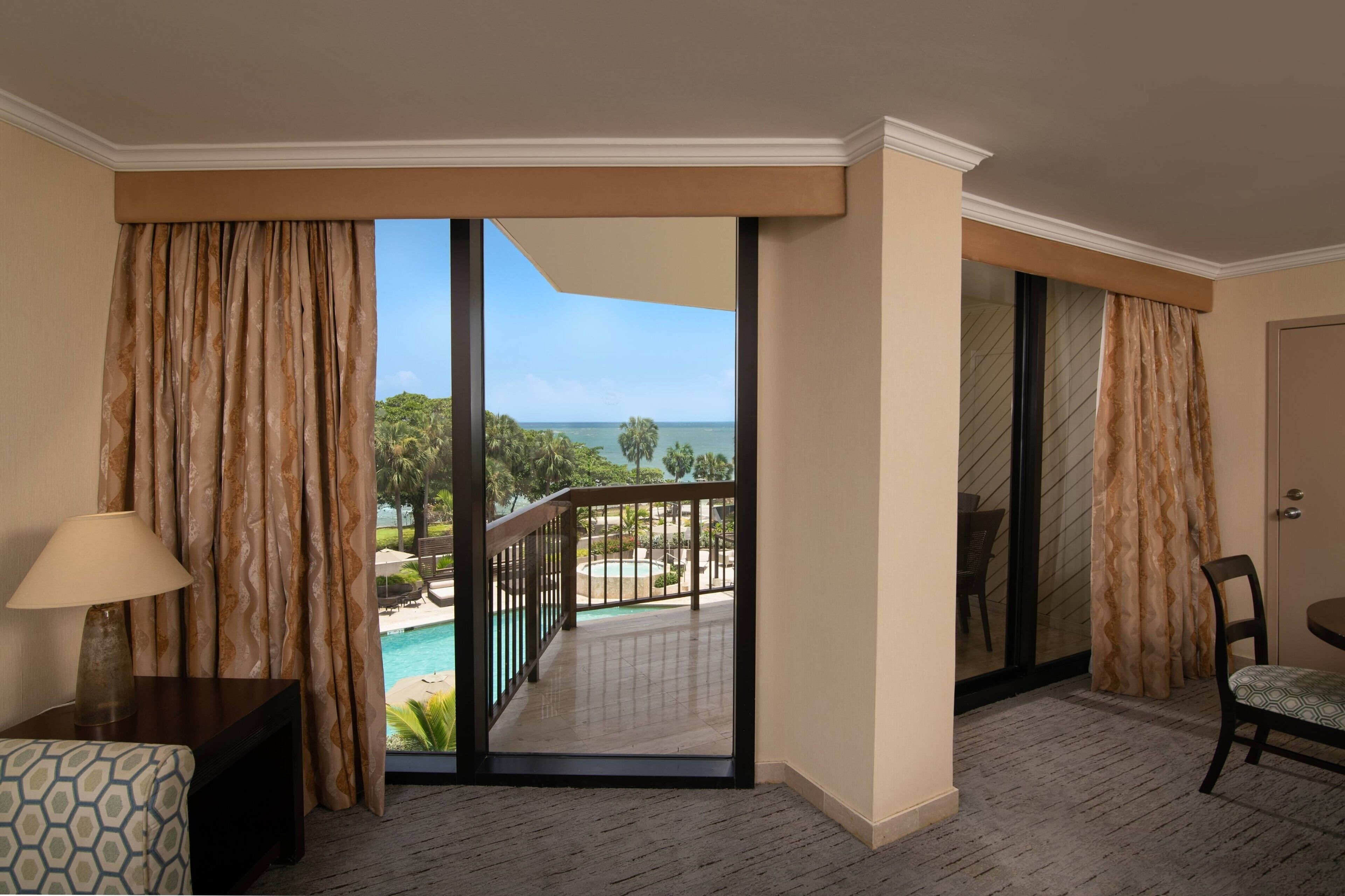 Quarto de hotel com vista para uma piscina e vegetação.