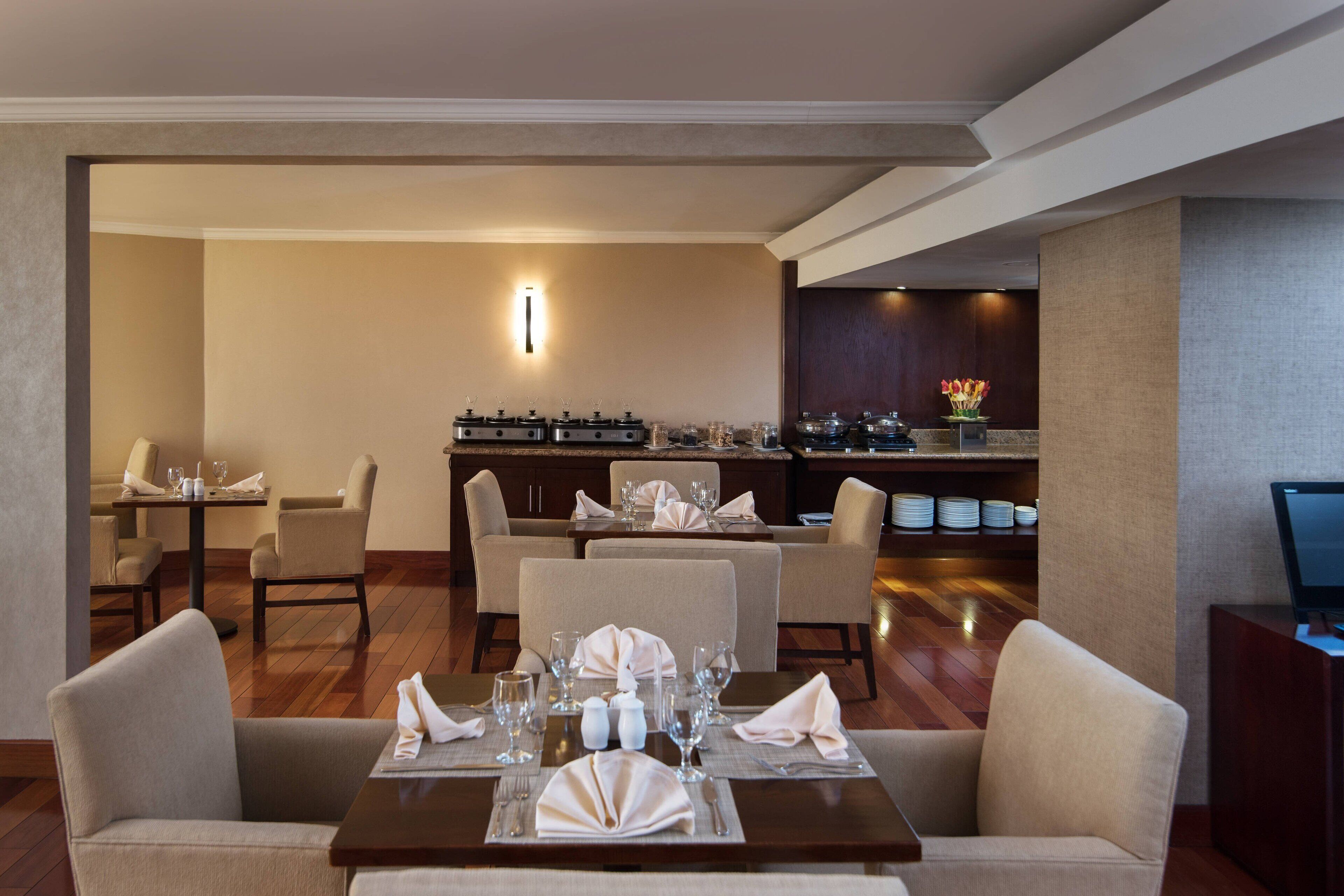 Un espace de restauration d’hôtel avec des tables dressées pour le service, un bar et un comptoir de réception.