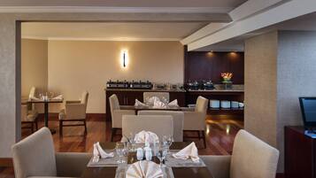 A hotel dining area with tables set for service, a bar area, and a reception desk.