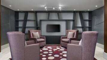 A modern living room with two armchairs, a patterned rug, and a flat-screen TV mounted on the wall.