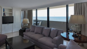 Una sala de estar moderna con sofá, mesa de centro y televisor. Cuenta con ventanas amplias con vista al mar.