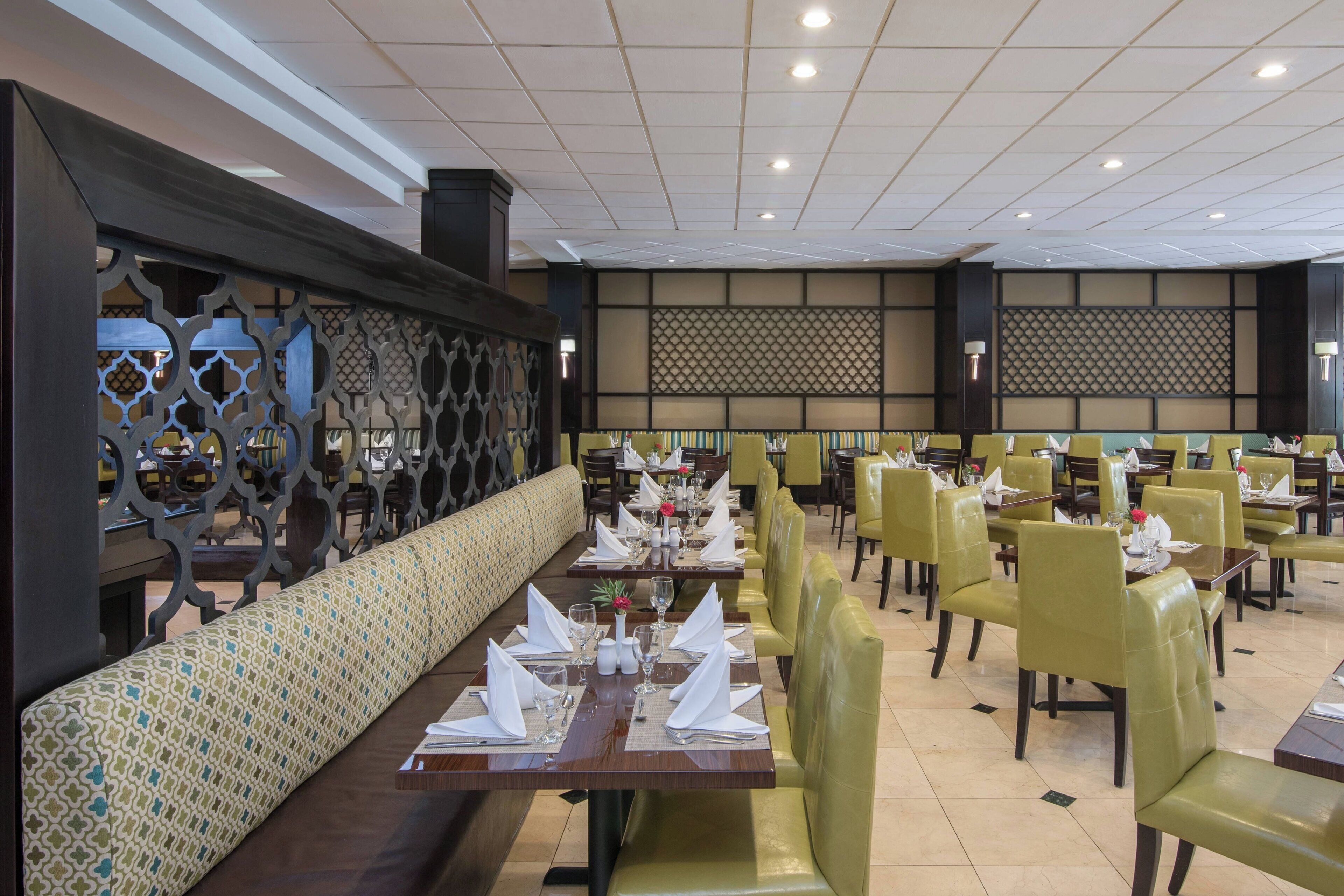 A restaurant with booths and tables, some with yellow cushions, and a patterned wall in the background.