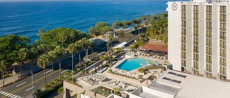 A hotel with a rooftop pool, a view of the ocean, and a parking area.