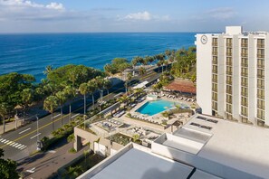 Un hotel con piscina en la azotea, vistas al océano y un área de estacionamiento.