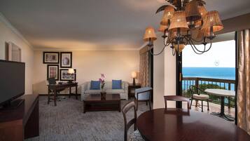 A hotel room with a living area, a dining table, a sofa, a TV, and a balcony with a view.