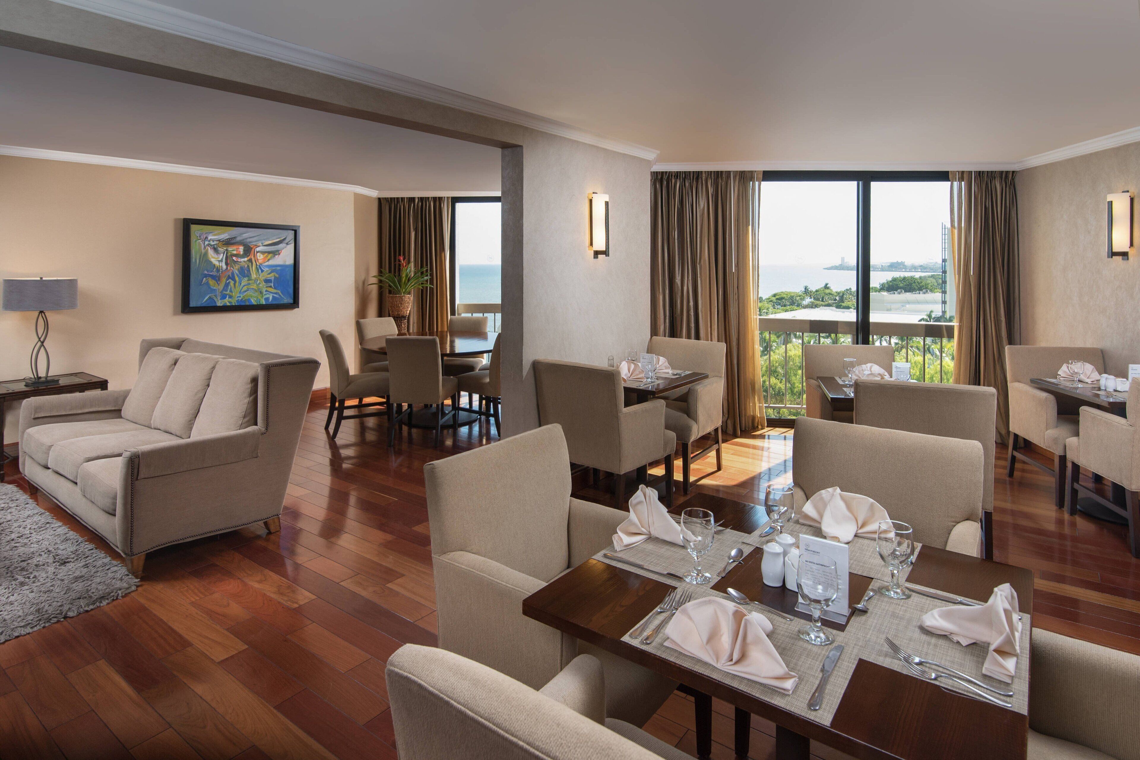 Habitación de hotel con comedor, sofá y vista al mar.