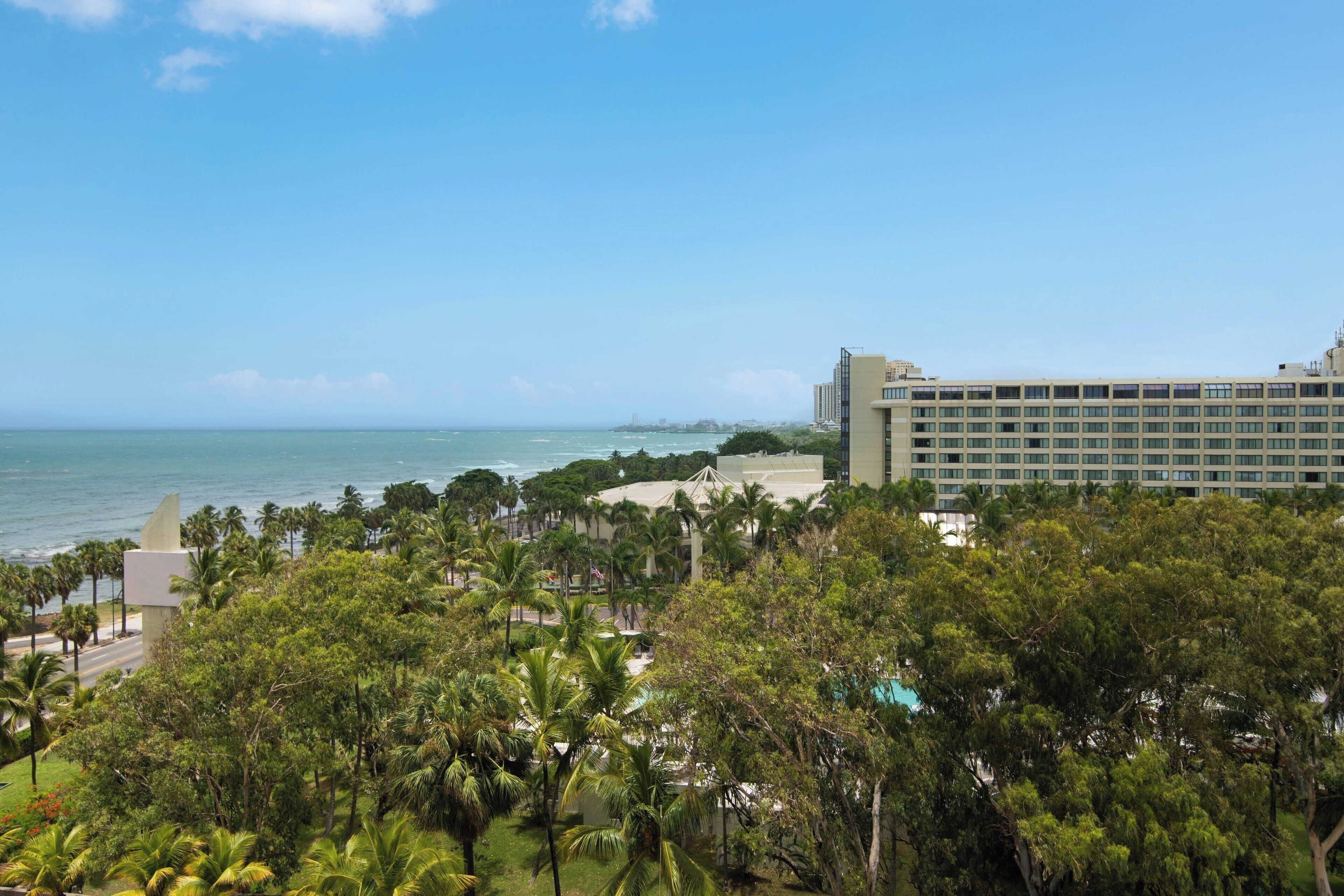 Um resort com vista para o oceano, palmeiras e um edifício grande com vários andares.