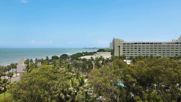 Um resort com vista para o oceano, palmeiras e um edifício grande com vários andares.