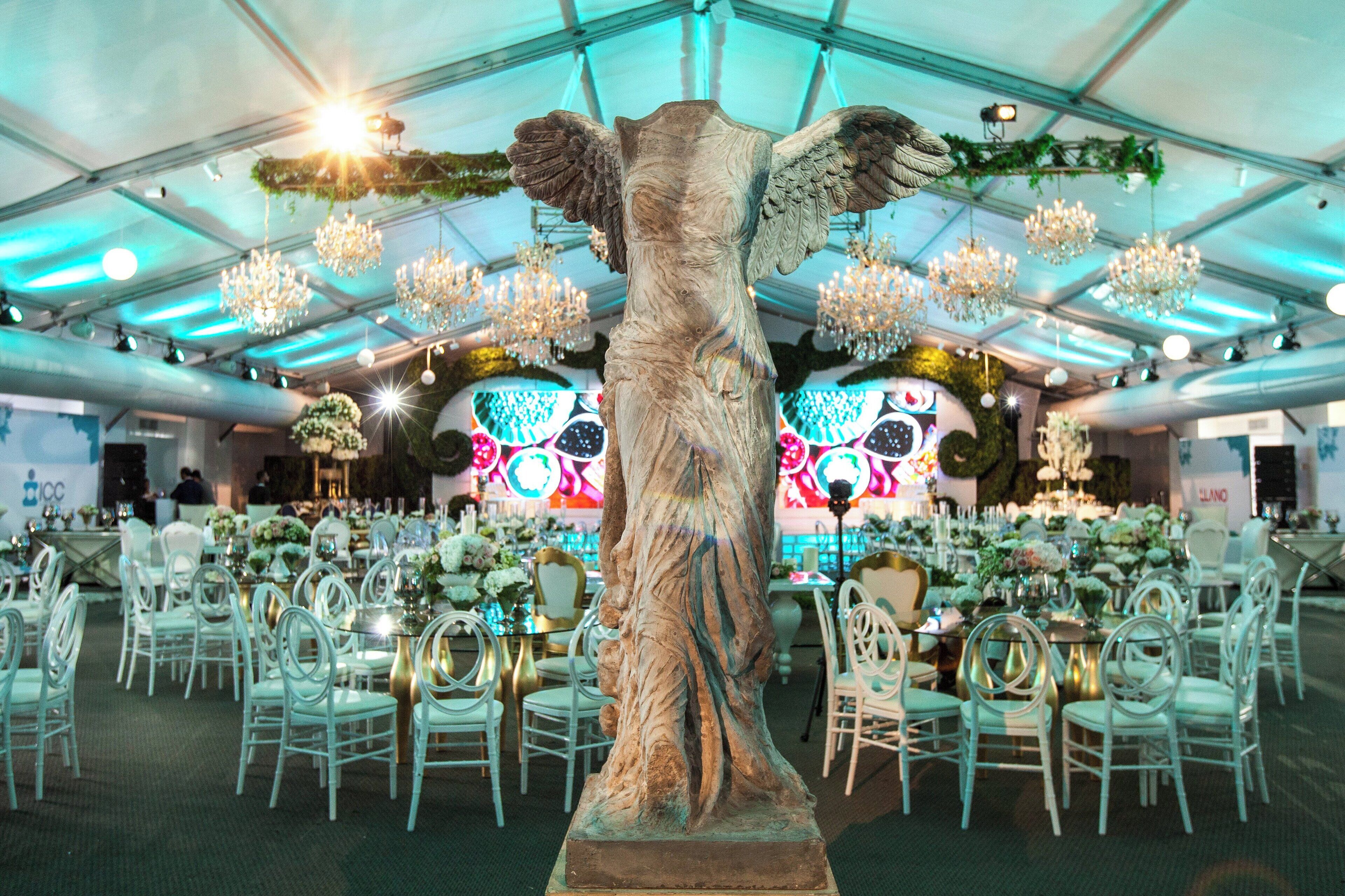 A banquet hall with white chairs, round tables, and a central decorative sculpture.