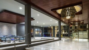 Un lobby amplio con una escalera de mármol, una zona de estar con sofás y un moderno candelabro.