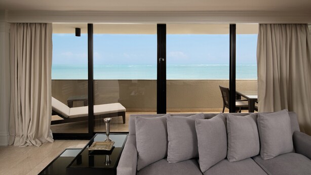 Una sala de estar moderna con un sofá gris, una mesa de centro y vistas a la playa a través de amplios ventanales.