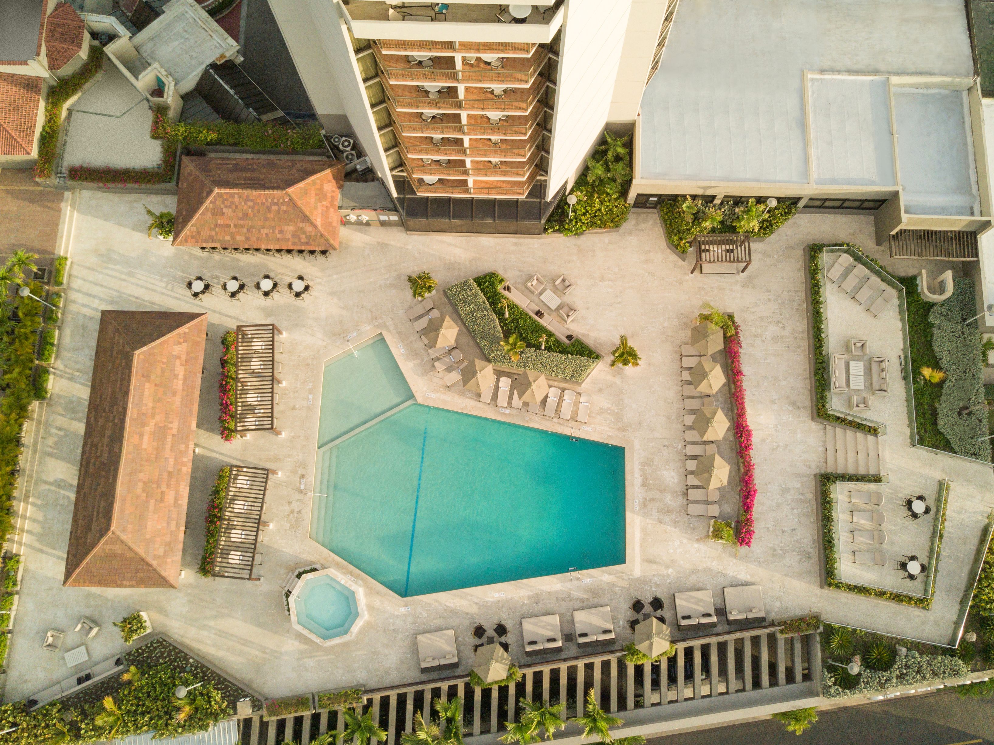 An aerial view of a resort with a large central pool, multiple lounge areas, and a variety of outdoor seating arrangements.