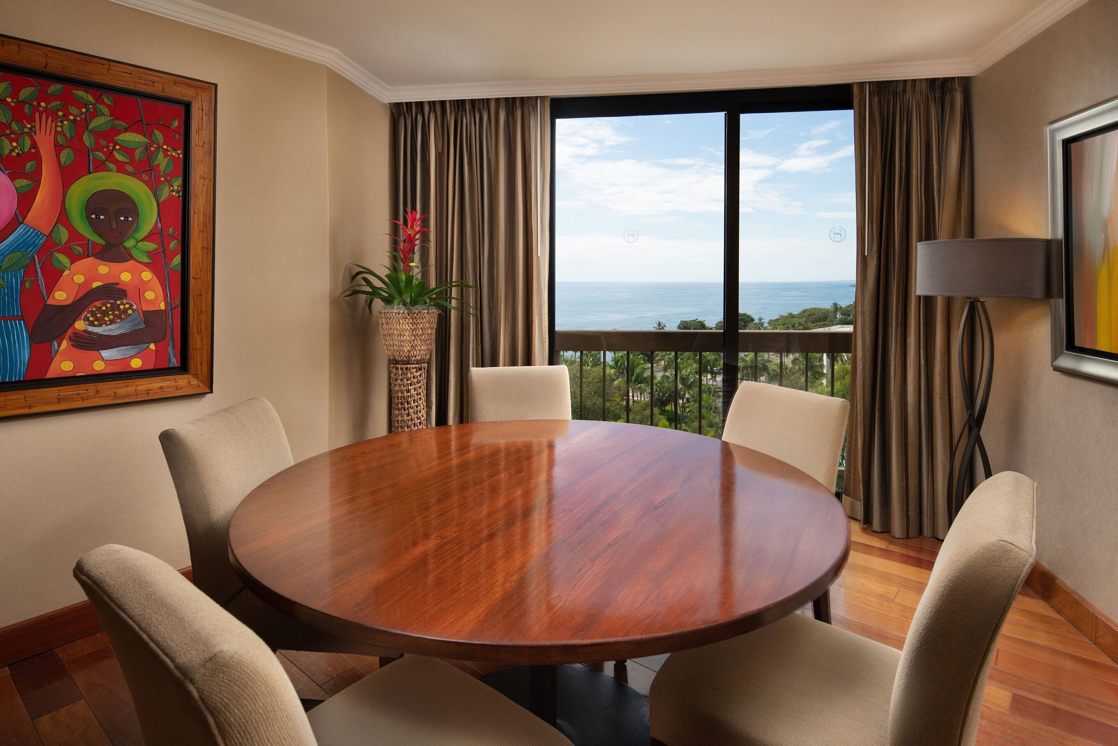 Un salón de conferencias con una mesa de madera y seis sillas, ventanas amplias con cortinas, una planta en maceta y un cuadro en la pared.