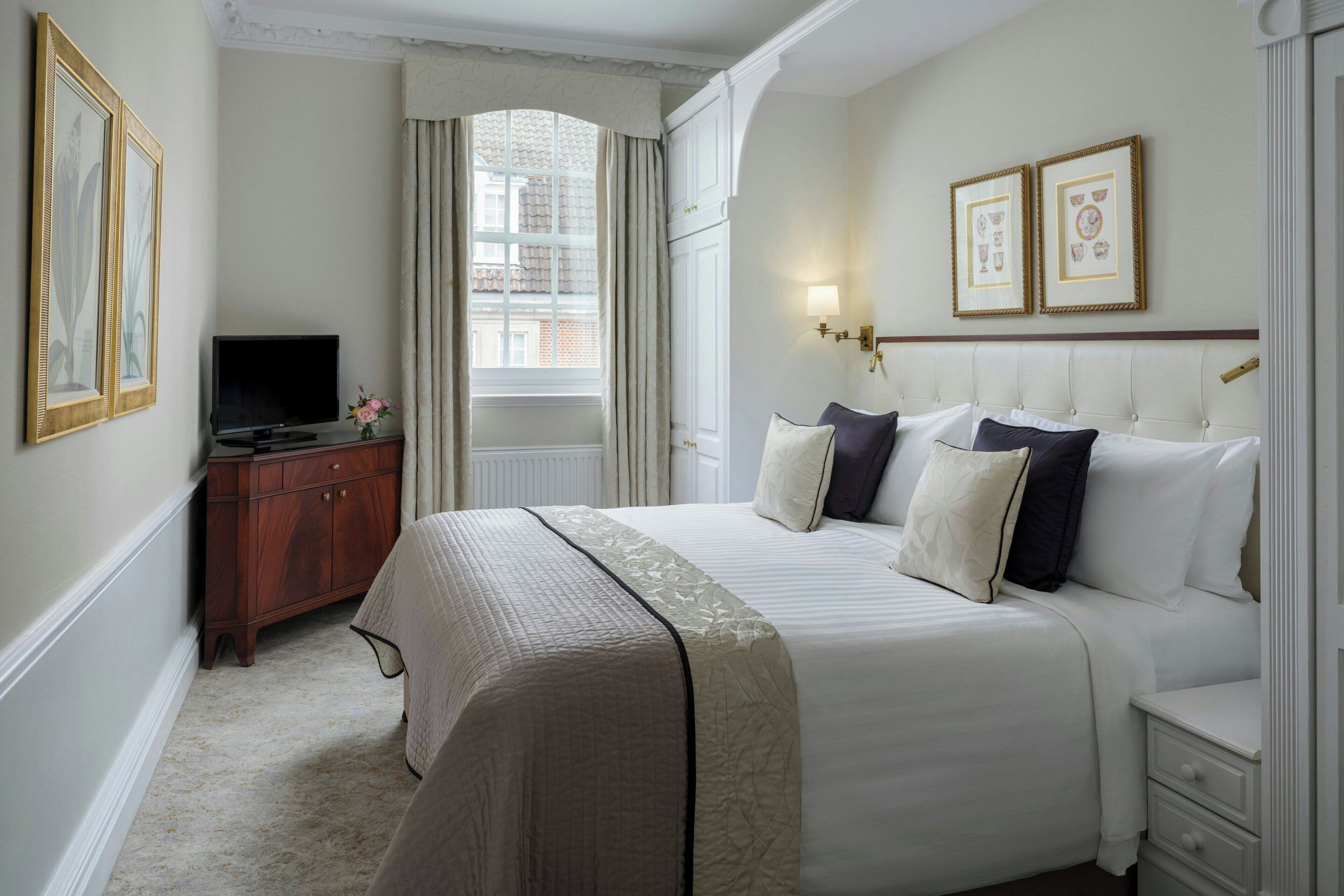 A hotel room with a bed, a TV, a dresser, and framed pictures on the wall.