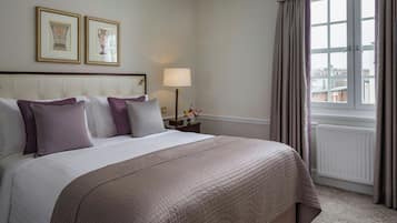 A hotel room with a large bed, a nightstand with a lamp, framed pictures on the wall, and a window with curtains.