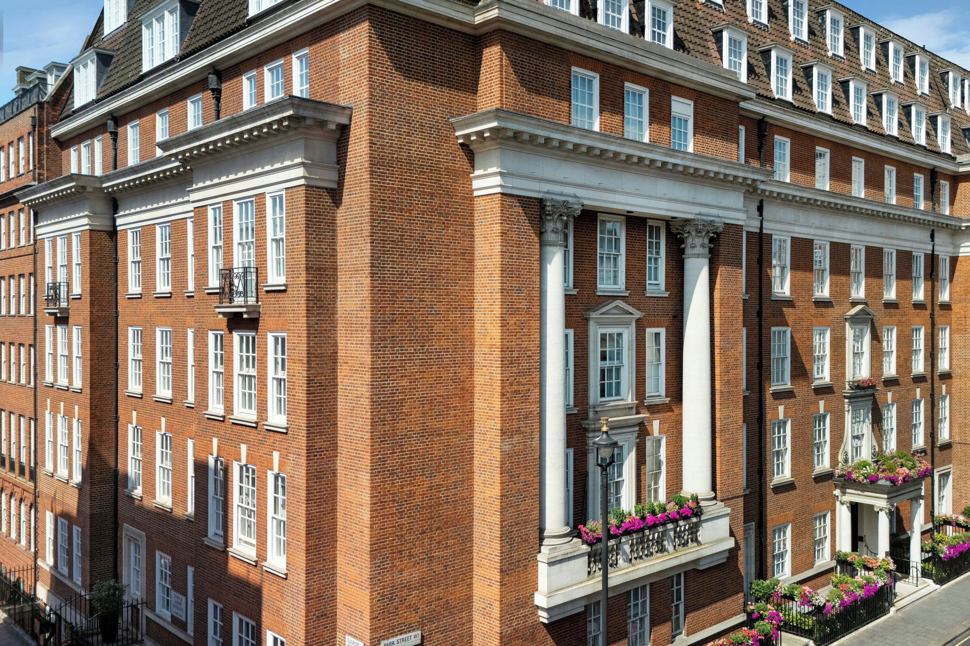 Un edificio de ladrillo de varios pisos con marcos de ventana blancos, una entrada central con una columna decorativa y un letrero que indica 'Park Street W1'.