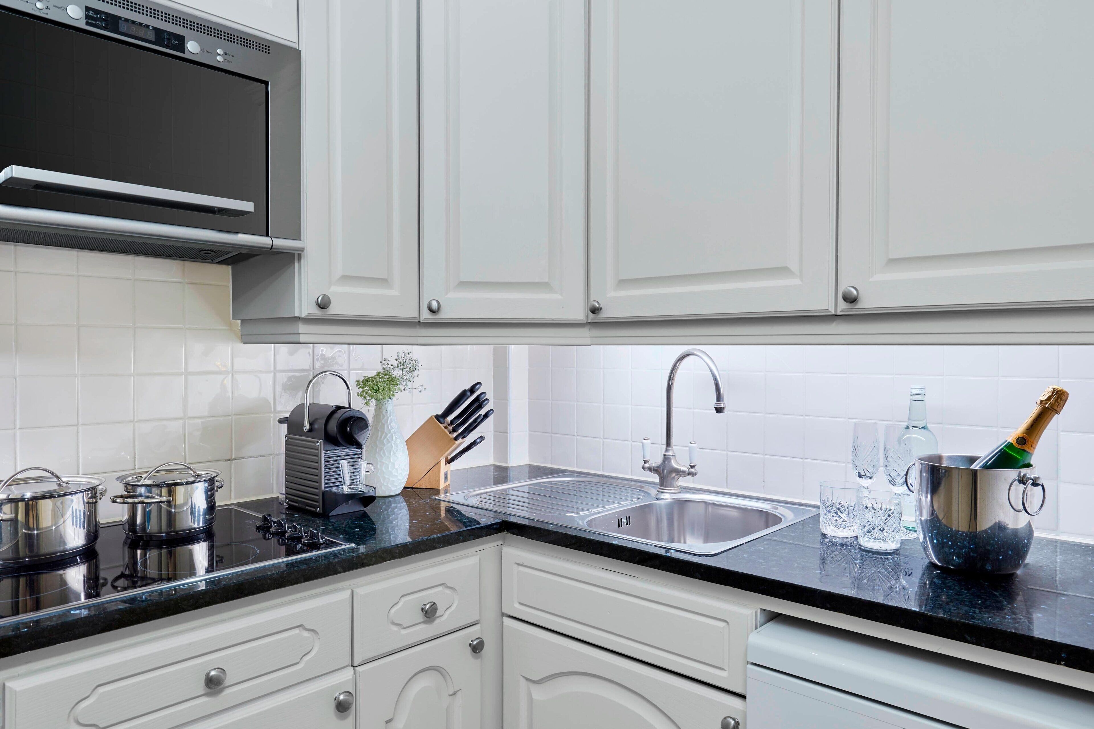A modern kitchen with white cabinets, a stainless steel sink, and a built-in oven.