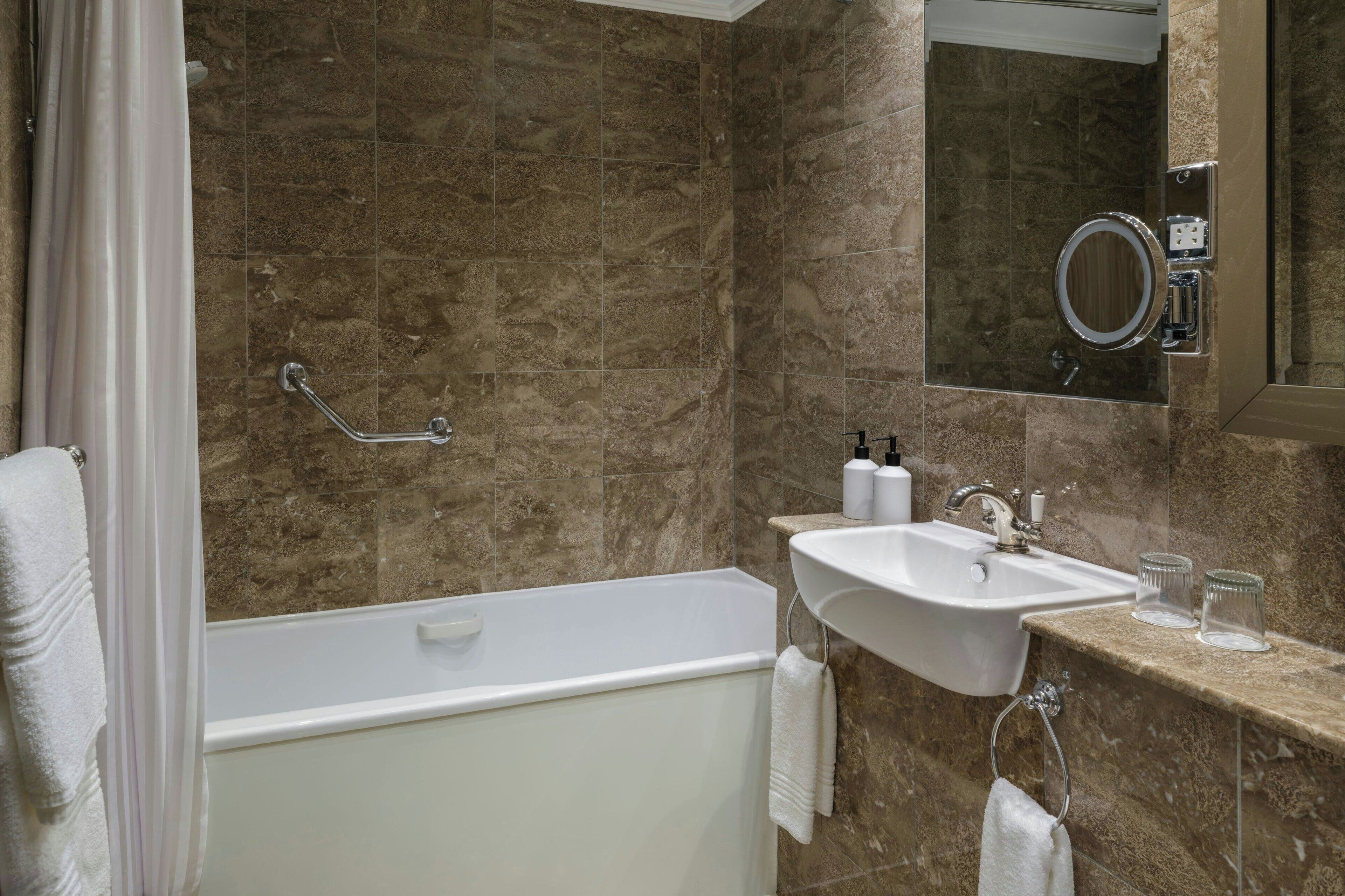 Ein Badezimmer mit Badewanne, Waschbecken, Spiegel und Handlauf.
