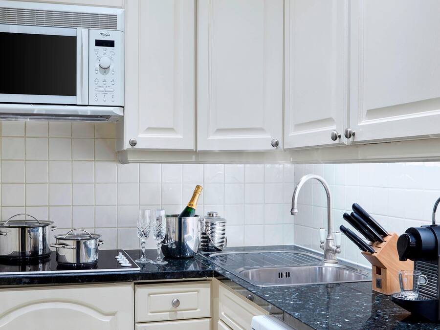 Una cocina con gabinetes blancos, un microondas, una estufa, un lavaplatos y un bloque de cuchillos.