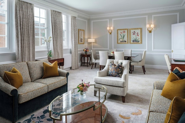 A living room with a sofa, armchair, glass coffee table, dining table with chairs, and a lamp. - 47 Park Street - Grand Residences by Marriott (London)
