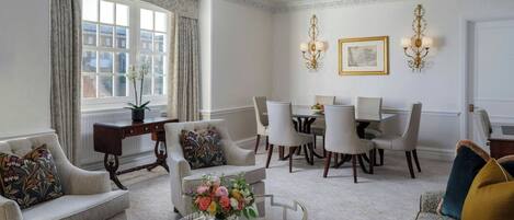 A room with a dining table, chairs, a sofa, a glass coffee table, and a window with curtains.