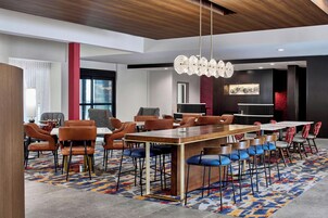 Un salón de conferencias moderno en un hotel, con una larga mesa, varias sillas y una alfombra estampada.